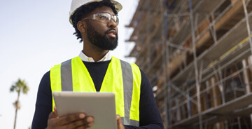Man holding a tablet on a job-site with construction vest on