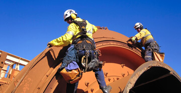 Two men on a job-site wearing safety gear working on a large vessel