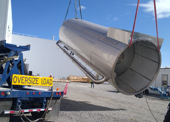 Large pipe being lowered on an oversize load bed for transportation at a client facility